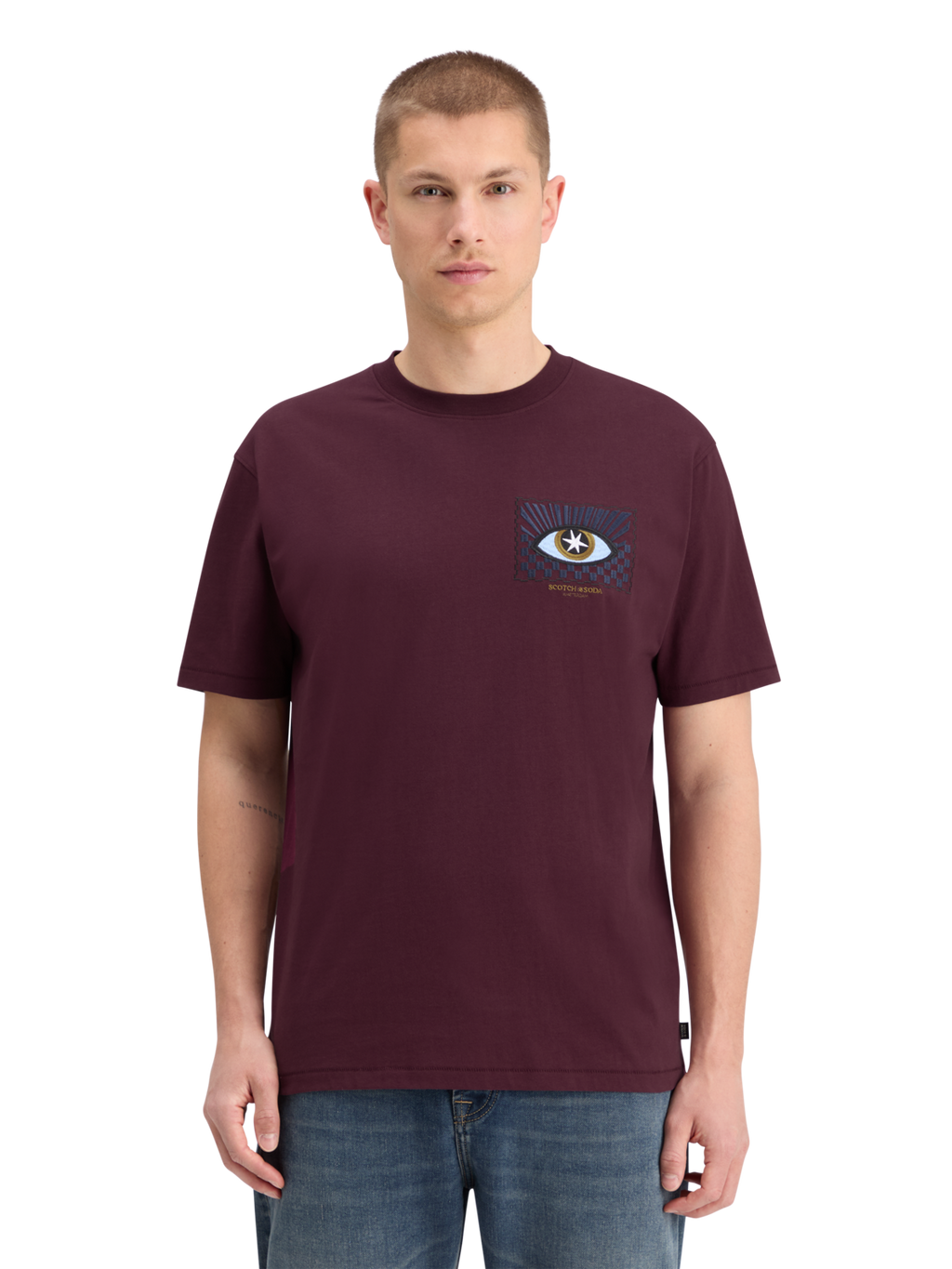 A man wearing a relaxed fit maroon t-shirt with front artwork, standing against a plain background.