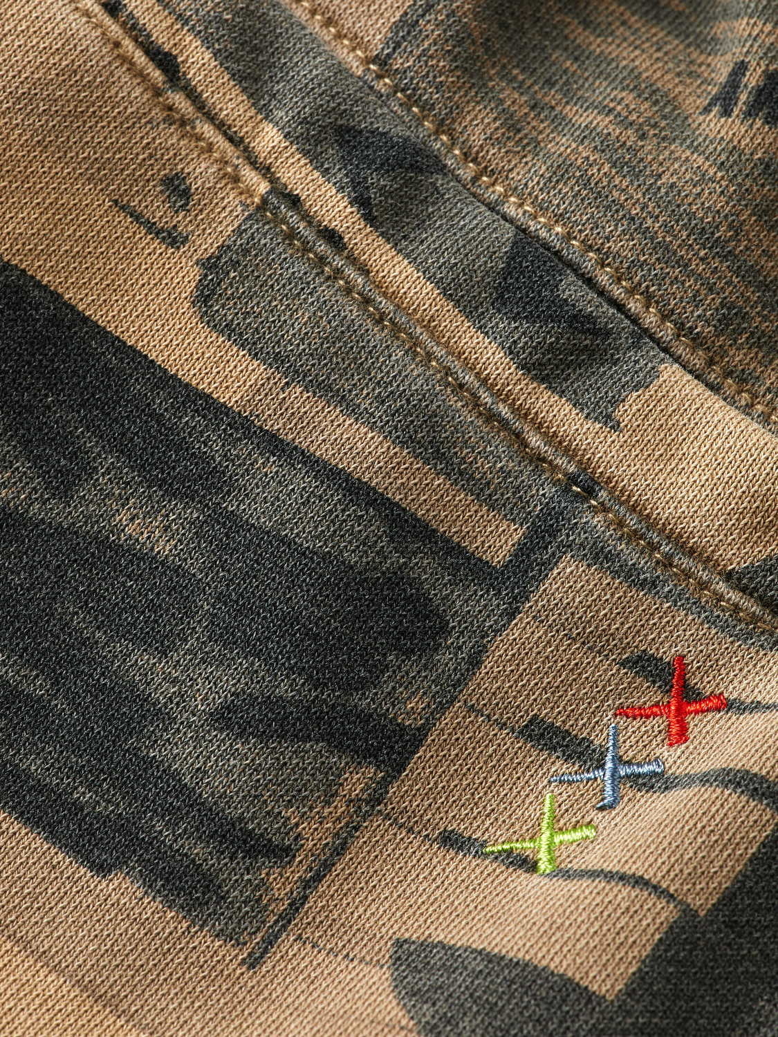 Close-up of a camouflage-patterned fabric with embroidered colorful arrows.