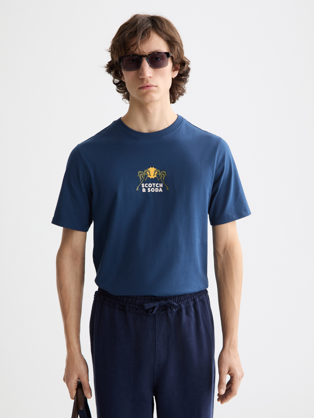 Man wearing a navy blue t-shirt with a logo and text, standing against a white background