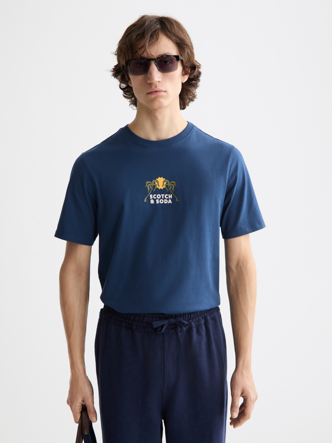 Man wearing a navy blue t-shirt with a logo and text, standing against a white background