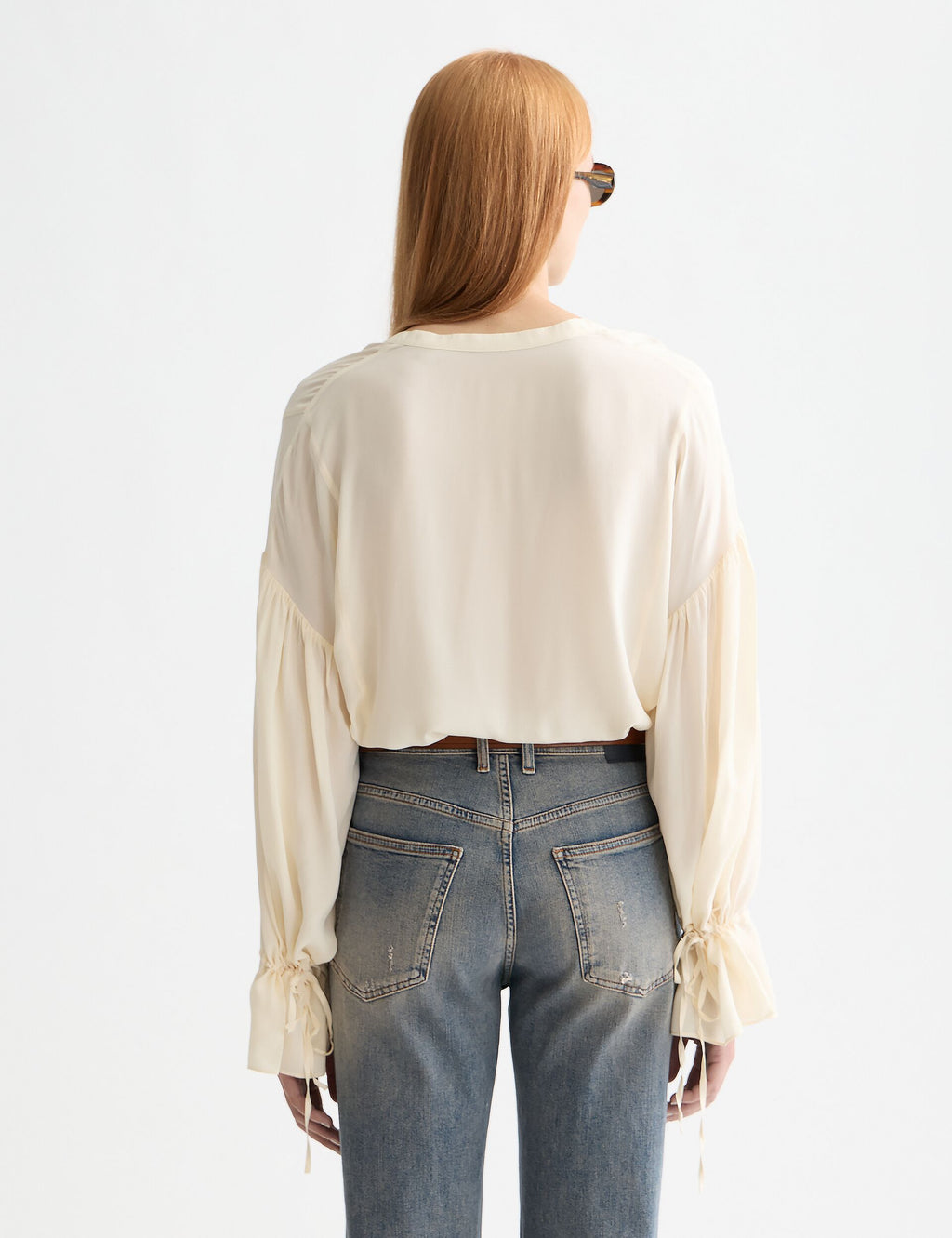 Person wearing a white blouse and blue jeans on a light gray background