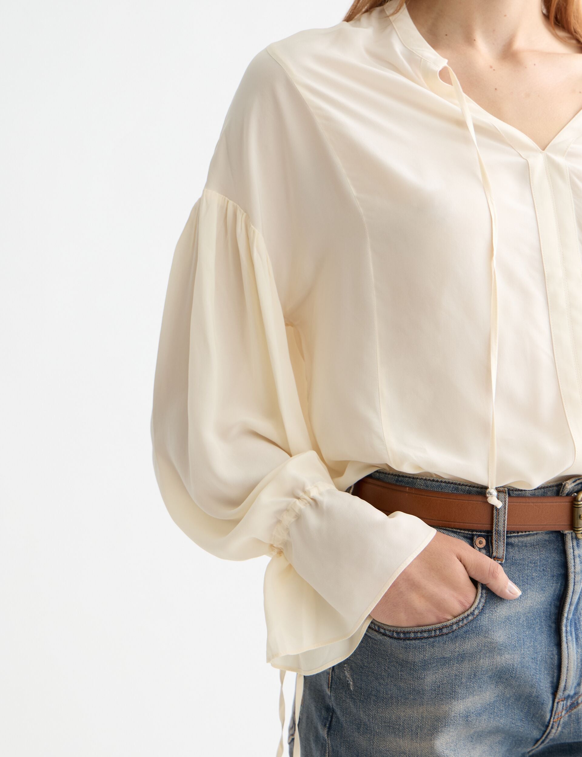 Person wearing a cream blouse with long sleeves and blue jeans on a white background