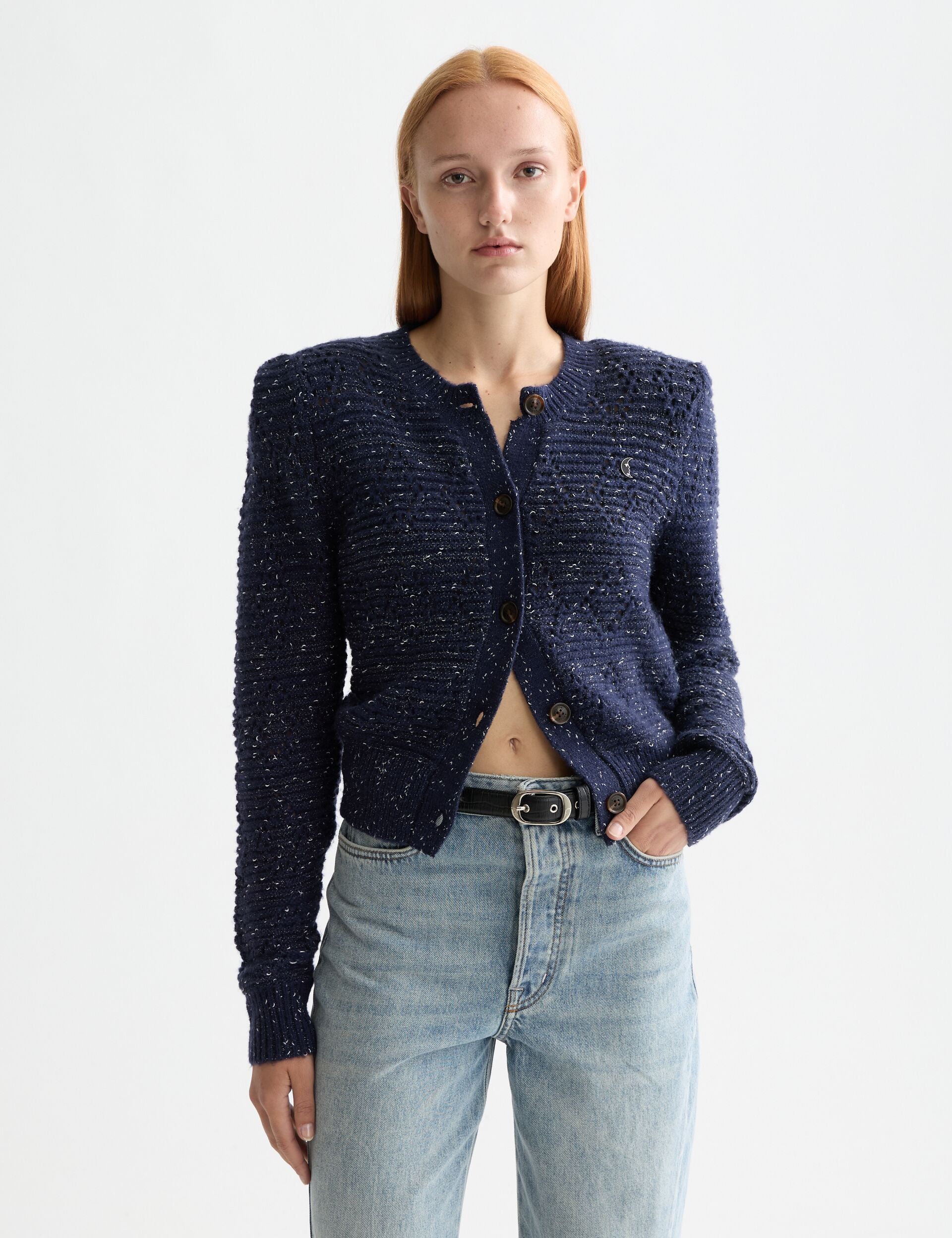 Person wearing a navy blue textured cardigan and light blue jeans on a white background