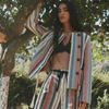 female model in stripe patterned pantsuit and bra posing in front of a tree